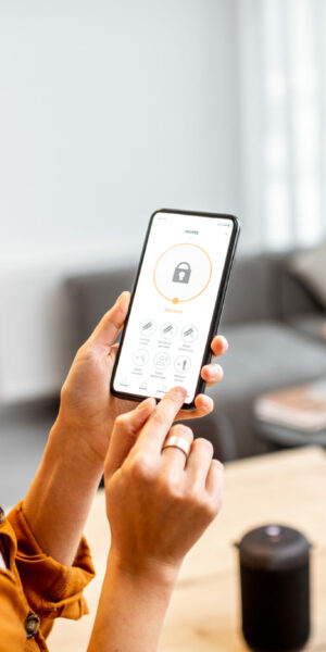 guest-adom-partenaire-minut-surveillez-votre-logement Young woman holding smart phone with launched security application at home. Concept of controlling and managing home security from a mobile device