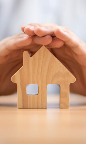 Wooden toy house protected by hands. Home insurance concept Wooden toy house protected by hands. Home insurance concept