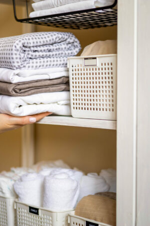 Domestic woman in pajamas neatly putting folded linens into cupboard vertical storage Marie Kondo Domestic woman in pajamas neatly putting folded linens into cupboard vertical storage system use Marie Kondo method. Female housewife spring seasonal cleaning space organizer with organized boxes